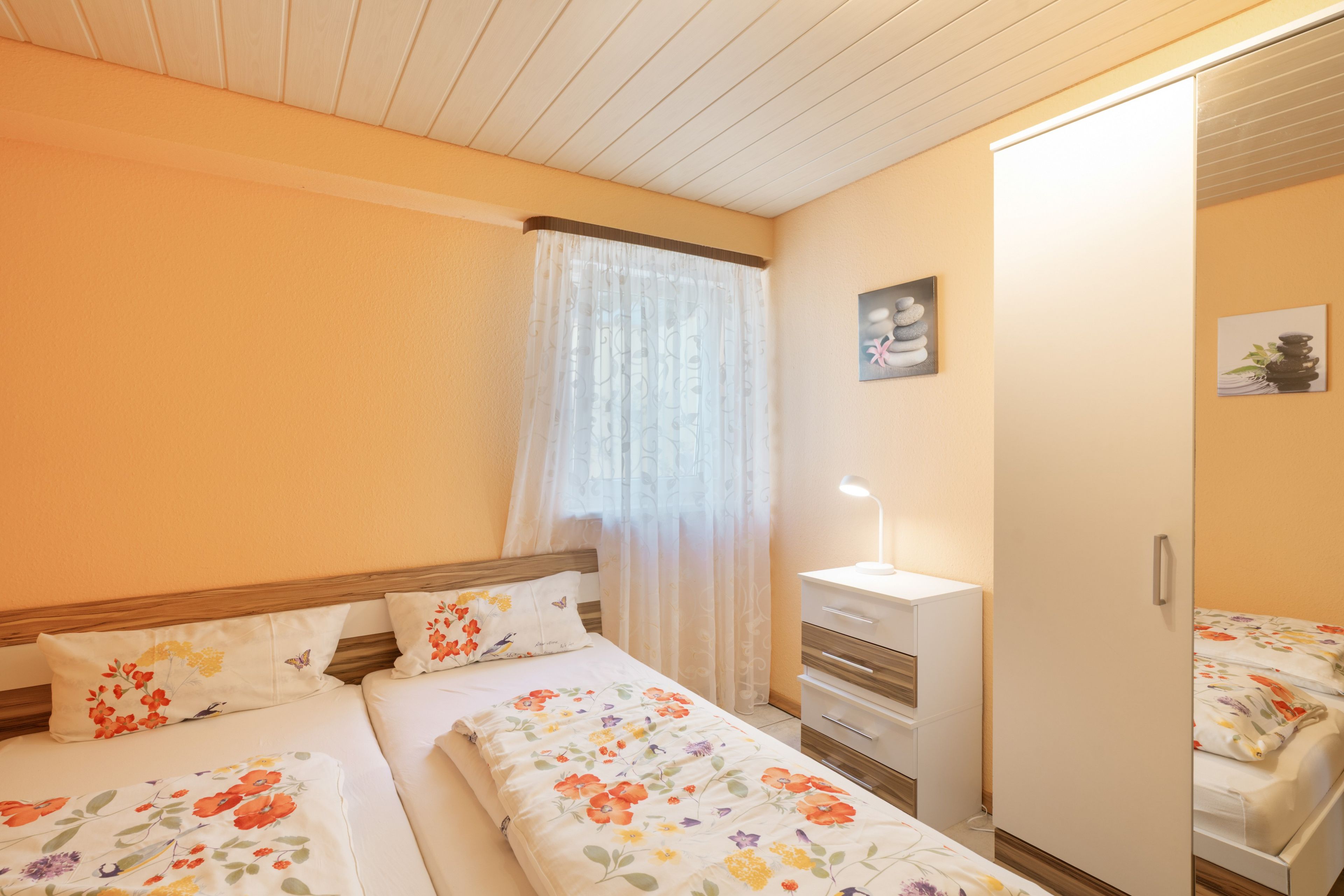 Habitació amb dos llits, un armari, una taula de nit amb una làmpada i una finestra amb cortines.