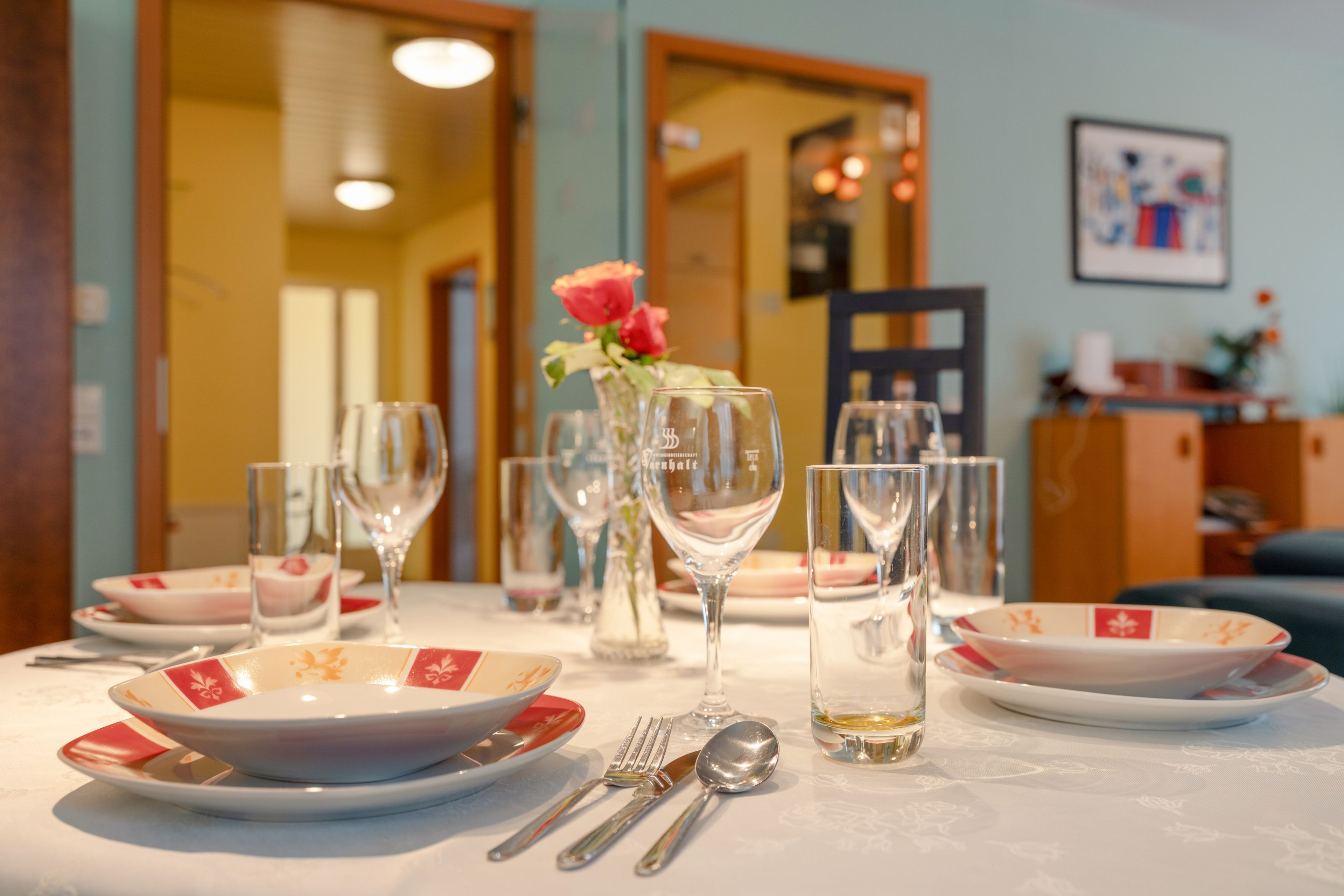Un tavolo da pranzo apparecchiato con piatti, bicchieri, posate e un vaso con fiori.
