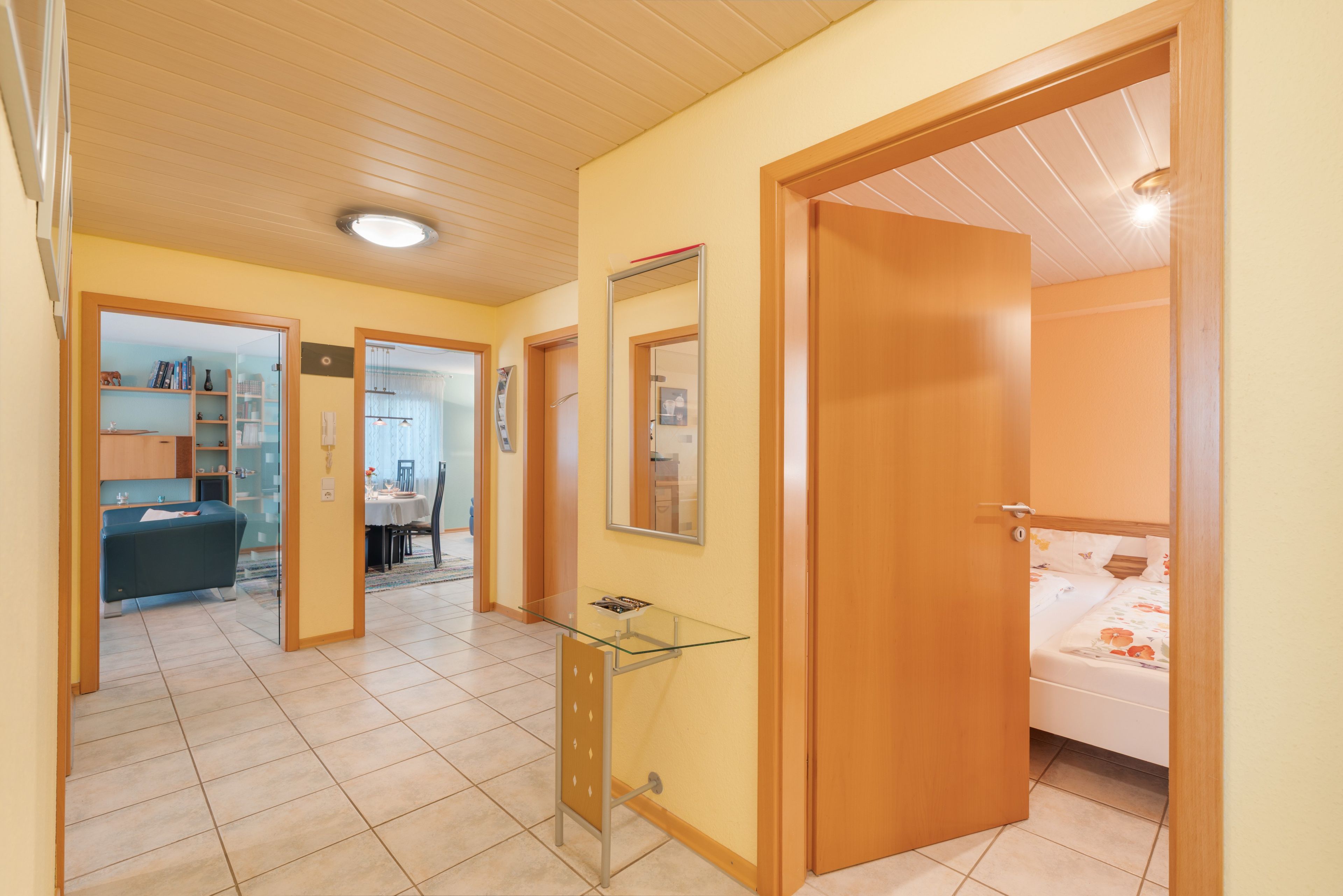 Een hotelkamer met een bed, nachtkastje en spiegel. Er is een deur naar een andere kamer.