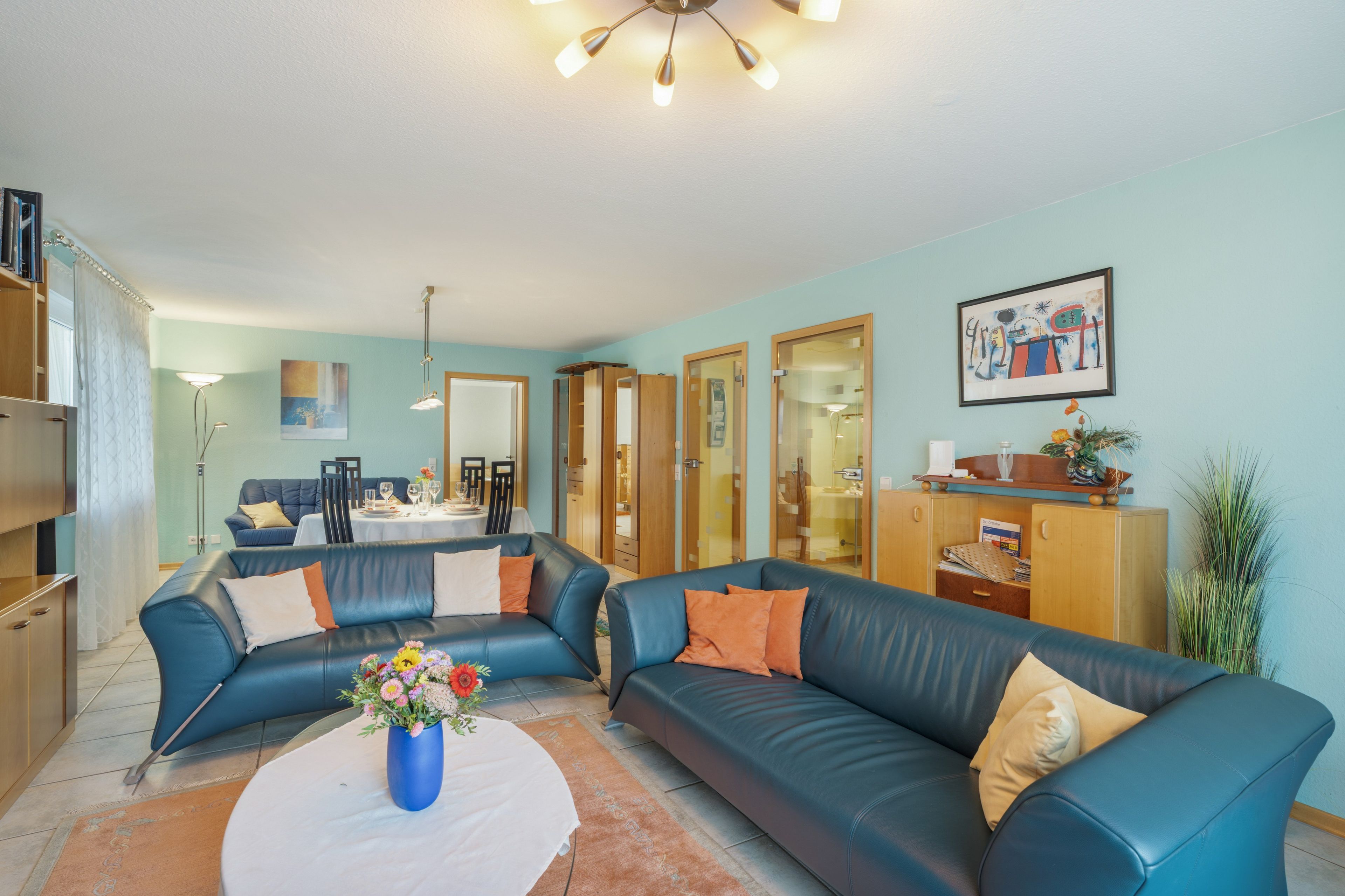 Ein Wohnzimmer mit einem blauen Ledersofa, einem Esstisch und einer Küchenzeile.