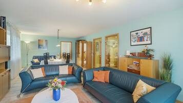 Ein Wohnzimmer mit einem blauen Ledersofa, einem Esstisch und einer Küchenzeile.