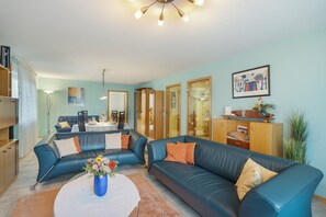 Een woonkamer met een blauwe leren bank, een eettafel en een keukenhoek.