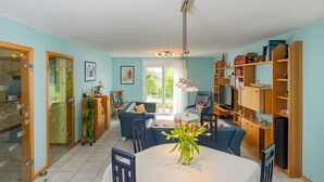 Uma sala de estar moderna com área de jantar, destacando uma mesa redonda, cadeiras, um vaso com flores e uma janela grande.