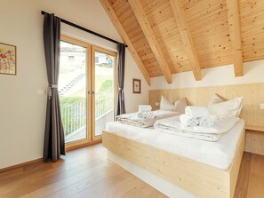 Ein Schlafzimmer mit Holzboden, einem Bett mit weißen Leinen und einer Glastür zu einem Balkon.