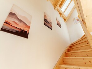 Eine Holztreppe mit einem Oberlicht, das zu einem Raum mit weißen Wänden und drei Landschaftsbildern führt.