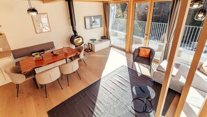 En modern inredning med ett träpanelat tak, en matplats med ett träbord och stolar, en soffa och en balkong med utsikt.