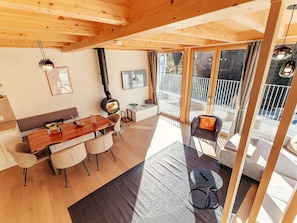 Ein modernes Interieur mit Holzboden, einem Essbereich mit Holztisch und -stühlen, einer Couch und einem Balkon mit Aussicht.