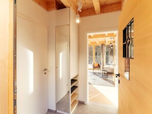 Un couloir avec une porte en bois, une bibliothèque intégrée et une vue sur un espace de vie comprenant un canapé et un fauteuil.