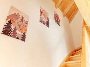 Eine Treppe mit Holzwerteln und einer weißen Wand, die drei gerahmte Kunstwerke zeigt, die abstrakte Berglandschaften darstellen.