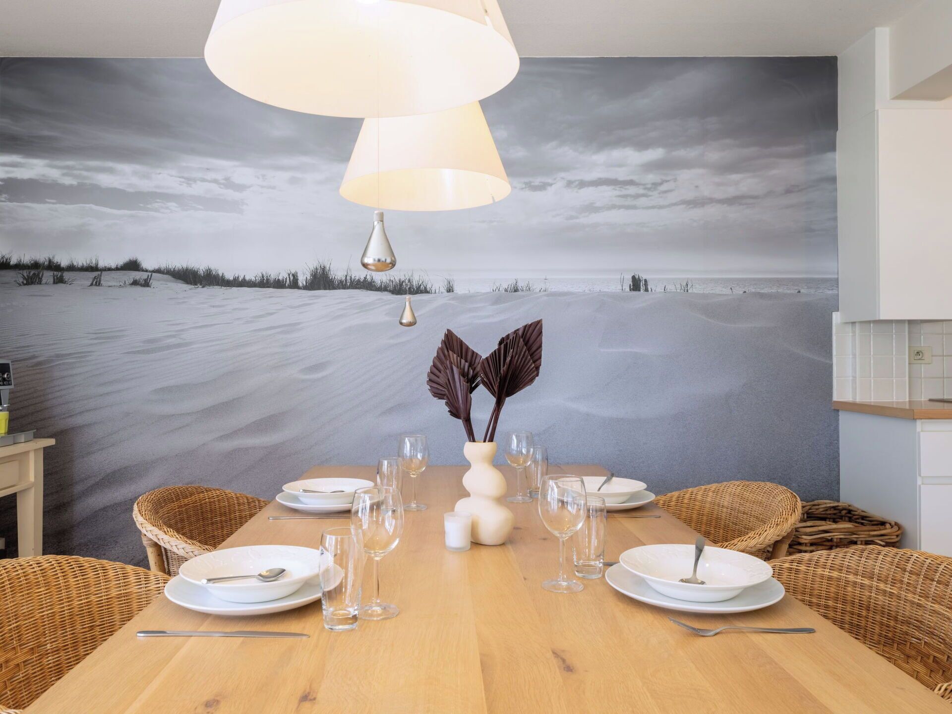 A dining area with a table set for four, a vase with decorative leaves, and a wall mural of a beach scene.