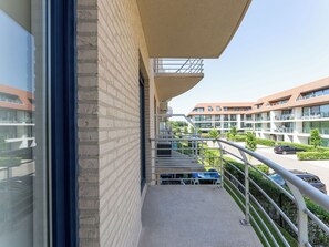 Ein Balkon mit Metallgeländer, freie Sicht auf einen Parkplatz und ein Gebäude mit zahlreichen Fenstern und Balkonen.