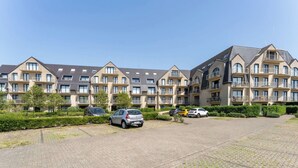 Ein mehrstöckiges Wohnhaus mit einem gepflasterten Innenhof und mehreren parkenden Autos vor der Fassade.