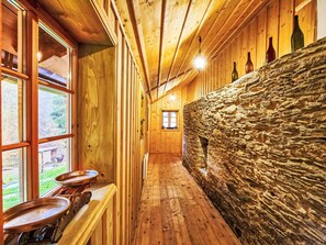 Ein schmaler Gang mit Holzwänden und einer Steinwand. Auf der linken Seite Fenster, am Ende eine Tür.