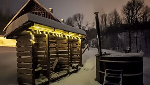 En stuga byggd av trä med ett snötäckt tak och en veranda med ljusslingor.