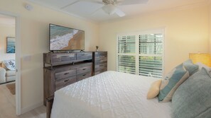 A bedroom with a bed, a dresser, a ceiling fan, a window with blinds, and a painting on the wall. - Charming 2-Bedroom Condo with Heated Pool – Perfect Monthly Retreat (Marco Island)