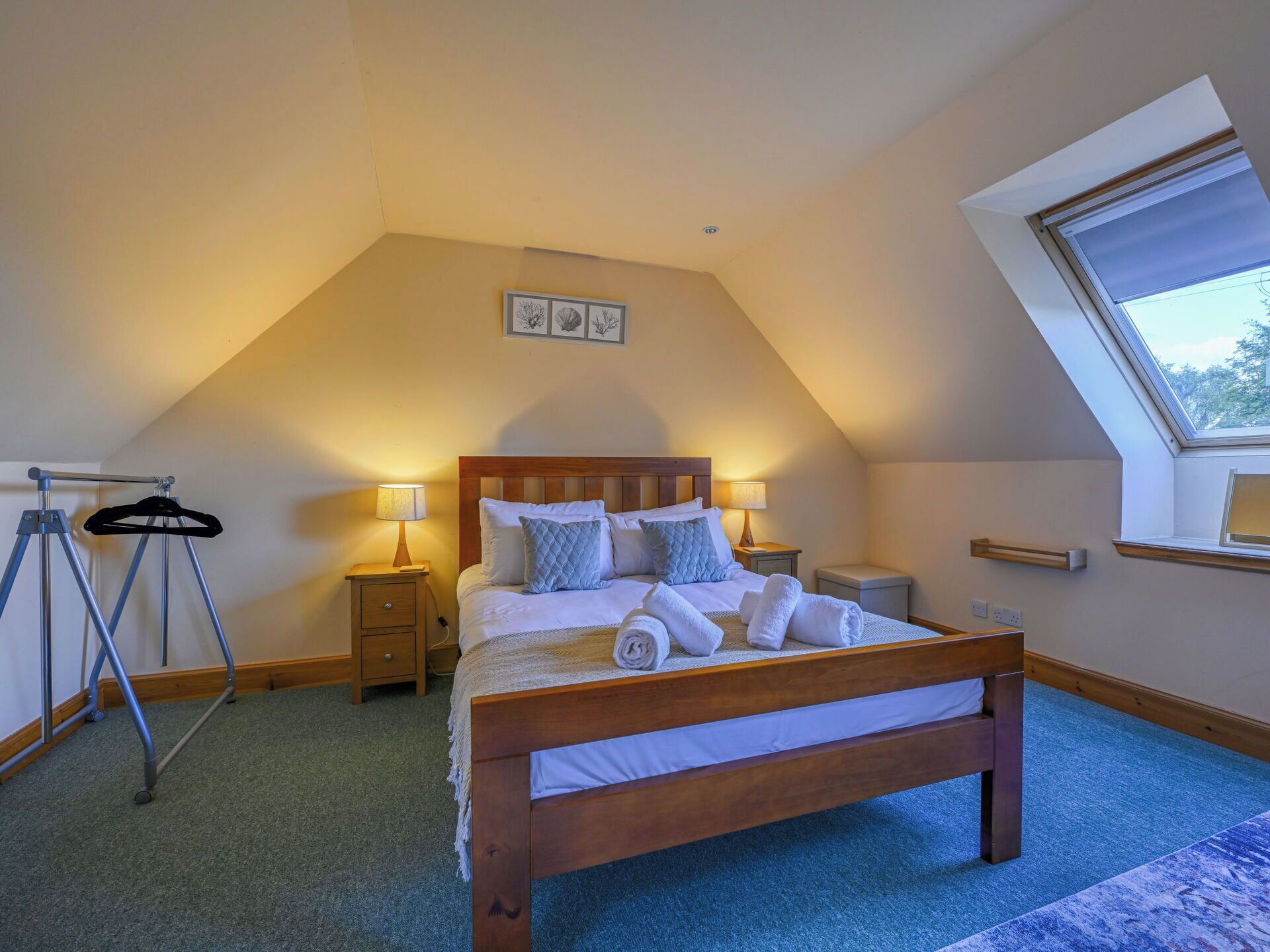 A bedroom with a sloped ceiling, a wooden bed, two bedside tables, a hanging rack, and a skylight.