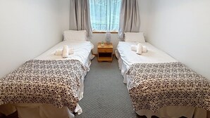 A room with two single beds, a small bedside table with a lamp, and a window with curtains.