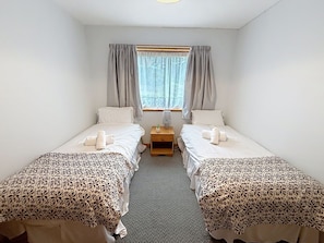 A room with two single beds, a small bedside table with a lamp, and a window with curtains.