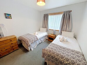 Een hotelkamer met twee enkele bedden, een houten dressoir, een nachtkastje, een lamp en een raam met gordijnen.