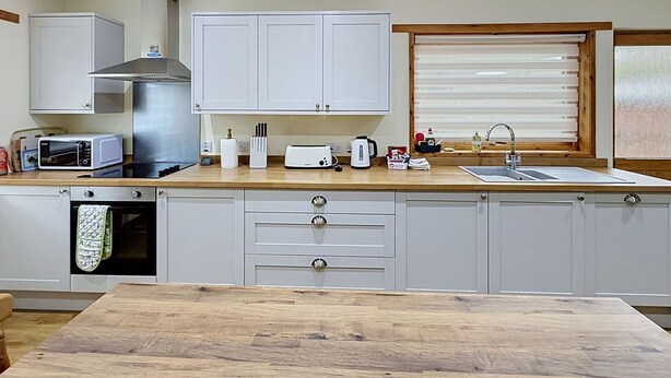 A modern kitchen with white cabinets, a stainless steel range hood, a microwave, a toaster, and a wooden countertop.