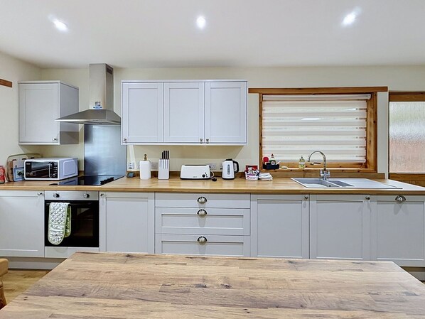 A modern kitchen with white cabinets, a stainless steel range hood, a microwave, a toaster, and a wooden countertop.