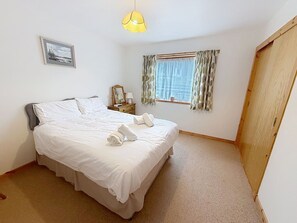 Ein Schlafzimmer mit Bett, Nachttisch, Lampe, einem Fenster mit Vorhängen und einer Tür.