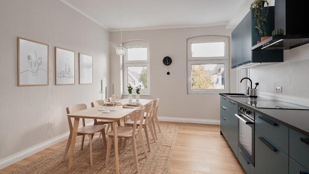 A modern kitchen with a dining area, wooden chairs, a rug, and a clock on the wall. - Saniertes Altbauzimmer an der Karlsaue (Kassel)