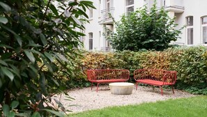 A garden area with two red metal benches and a round stone table, surrounded by greenery and a hedge. - Saniertes Altbauzimmer an der Karlsaue (Kassel)