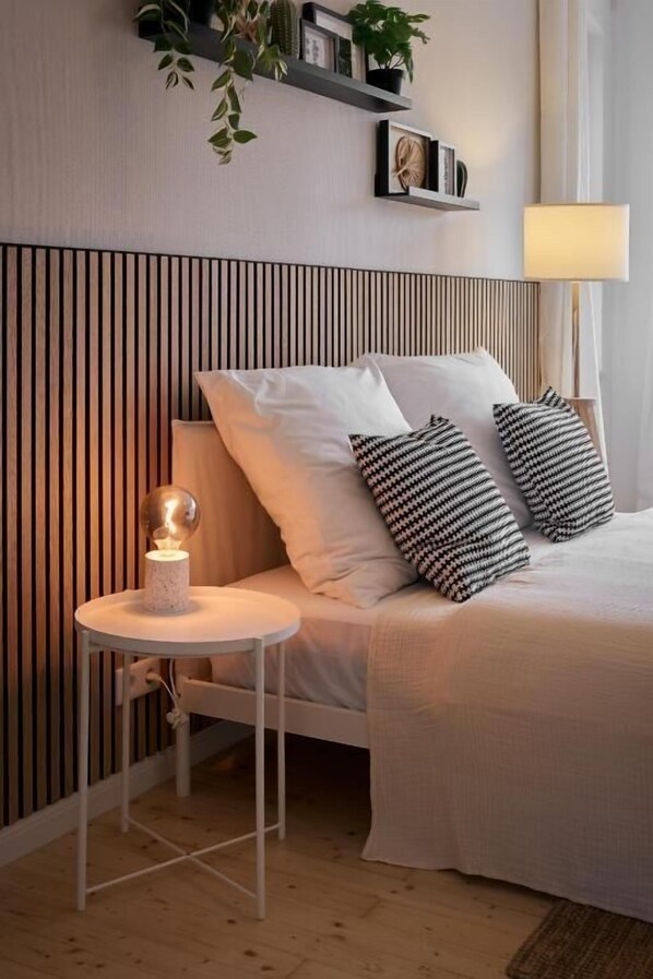Quarto bem arrumado com cama, luminária de cabeceira e uma mesinha com um objeto decorativo.