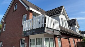 Een huis met twee verdiepingen, een witte picket fence, een balkon en een pannendak.