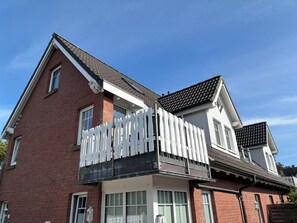 A two-story house with a white picket fence, a balcony, and a tiled roof. - 26 West – Duplex for 4, Westerland, 2 bathrooms, west-facing balcony, 10 min. to the beach (Sylt)