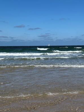 A beach with waves and a sailboat in the distance. - 26 West – Duplex for 4, Westerland, 2 bathrooms, west-facing balcony, 10 min. to the beach (Sylt)
