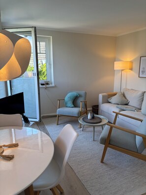 Una sala de estar moderna con un sofá blanco, un sillón gris, una mesa de centro redonda y una mesa de comedor con sillas.