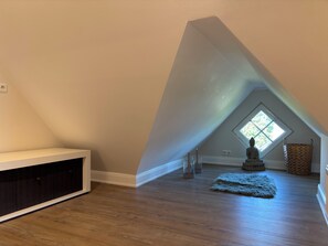 A room with a sloped ceiling, a built-in bench, a statue, a window, and a woven basket. - 26 West – Duplex for 4, Westerland, 2 bathrooms, west-facing balcony, 10 min. to the beach (Sylt)