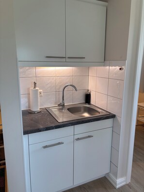 A kitchen with a stainless steel sink, white cabinets, and a marble countertop. - 26 West – Duplex for 4, Westerland, 2 bathrooms, west-facing balcony, 10 min. to the beach (Sylt)