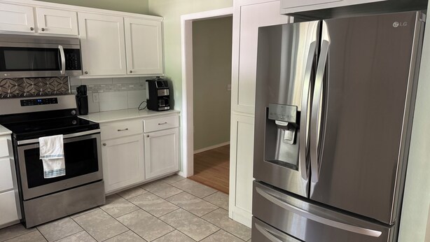 Una cocina moderna con electrodomésticos de acero inoxidable, armarios blancos y piso de baldosas.