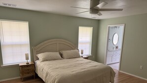 Un dormitorio con una cama, dos mesitas de noche, un ventilador de techo y una puerta que da a un baño.