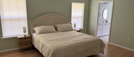 A bedroom with a bed, two bedside tables, a ceiling fan, and a door leading to a bathroom.