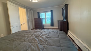 Een slaapkamer met een bed, een dressoir, een raam met gordijnen en een plafondventilator.