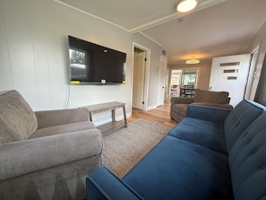 Ein Wohnzimmer mit einem an der Wand montierten Flachbildfernseher, einem grauen Sofa, einem blauen Sofa und einem Holztisch.