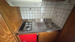 A compact kitchen with a gas stove, a sink, and a red cabinet. - Podere Valborgina (Castiglione della Pescaia)