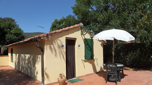 A small building with a tiled roof, a door, a window with a green shutter, and a patio area with a table and chairs. - Podere Valborgina (Castiglione della Pescaia)