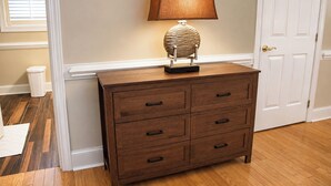 Een houten dressoir met zes lades en een lamp erboven, geplaatst tegen een muur met een deur aan de rechterkant.
