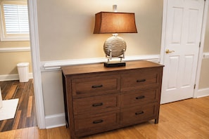 A wooden dresser with six drawers and a lamp on top, positioned against a wall with a door to the right.
