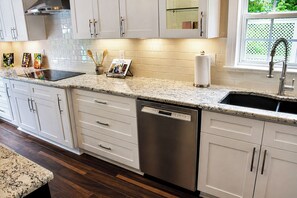 A modern kitchen with white cabinetry, a stainless steel dishwasher, and a granite countertop.