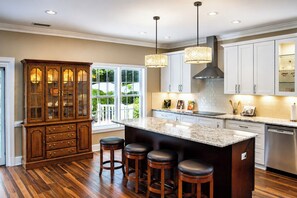 A kitchen with a large island, wooden bar stools, and a cabinet with glass doors. - The Cary Retreat • Luxury Cottage in the Heart of Downtown Cary (Cary)