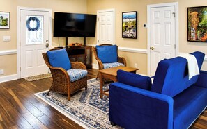 A living room with a television, two wicker chairs with blue cushions, a blue sofa, and a patterned rug.