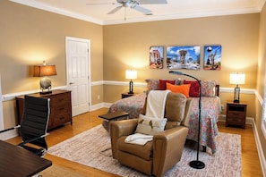 A bedroom with a bed, a chair, a desk, a lamp, and artwork on the wall.