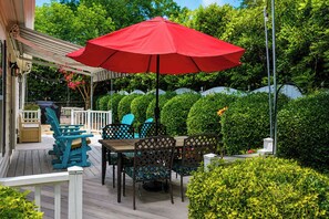 A wooden deck with a table and chairs, a red umbrella, and a white railing.