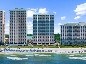 Ein Strandhotel mit mehreren Hochhäusern, einem Sandstrand mit Sonnenschirmen und dem Meer.